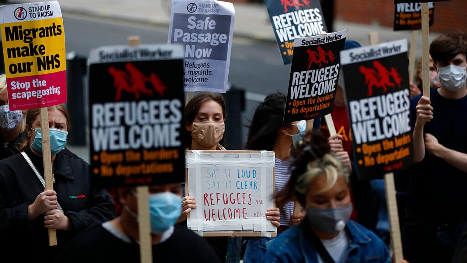 Protestors hold placards during a pro-migrants protest outside the government's Home Office in London, Tuesday, Aug. 25, 2020