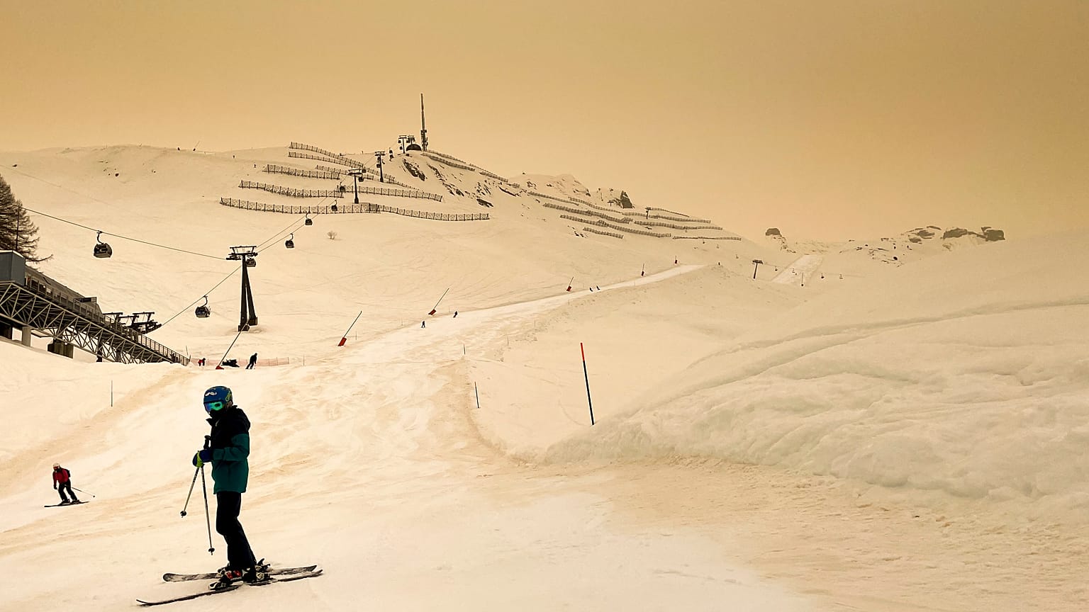Skiers wearing protective face mask ski as Sahara sand colours the snow and the sky in orange in Anzere, Switzerland, on February 6 2021.