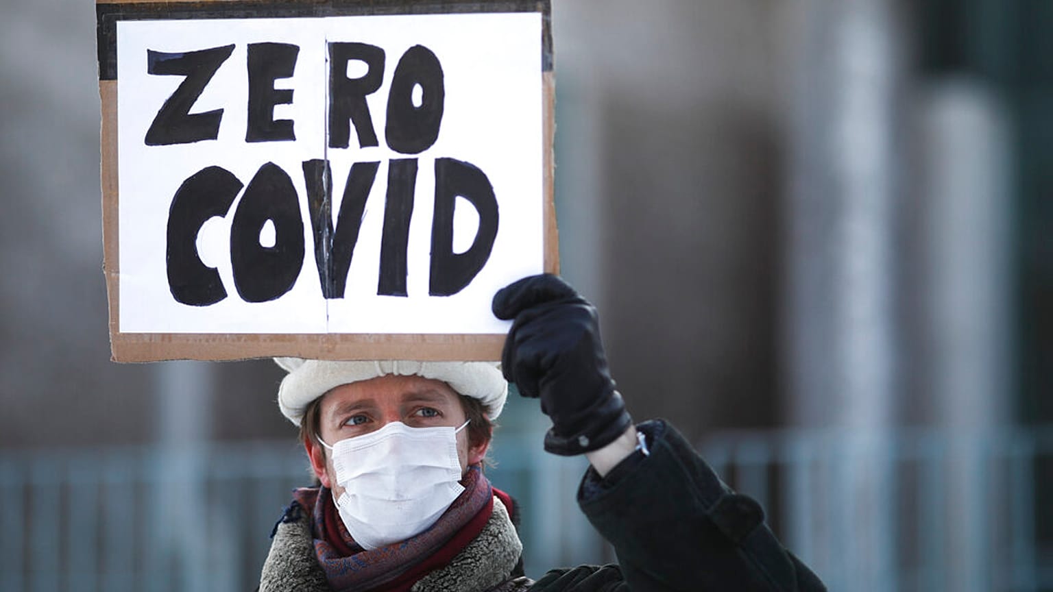A demonstrator holds up a poster that reads: 'Zero COVID' in front of the chancellery in Berlin, Wednesday, Germany, Feb. 10, 2021, as he attends a protest.