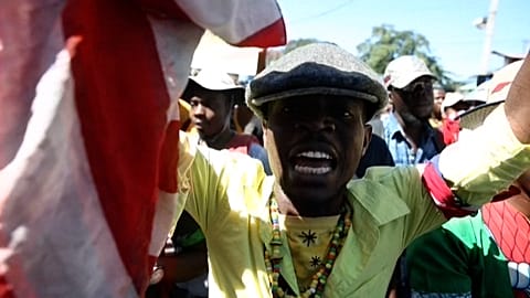 Demonstrator holds a copy of the Haitian Constitution wrapped in an American flag 