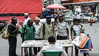 موطنون تنزانيون يقفون أمام بائع جرائد من دون التقيد بإجراءات التباعد الاجتماعي للحد من انتشار فيروس كورونا 