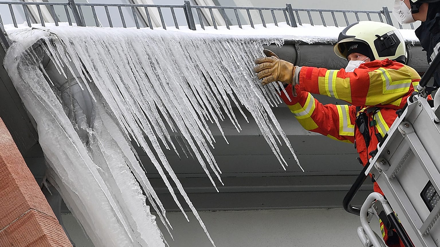 Firefighters break large icicles from the gutter of a house in the city centre of Erfurt, Germany, Thursday, Feb.11, 2021. 