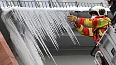 Firefighters break large icicles from the gutter of a house in the city centre of Erfurt, Germany, Thursday, Feb.11, 2021. 