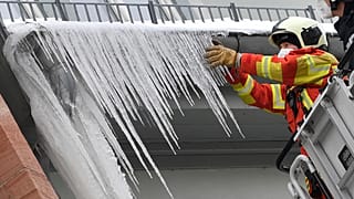 Firefighters break large icicles from the gutter of a house in the city centre of Erfurt, Germany, Thursday, Feb.11, 2021. 