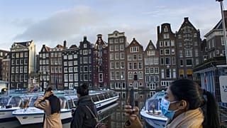 A woman, wearing a face mask to curb the spread of the COVID-19 virus, takes images of empty and moored canal cruise boats docked in Amsterdam, Netherlands, Thursday, Feb. 4,