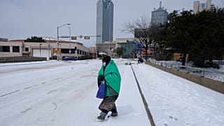 A woman wrapped in a blanket crosses the street near downtown Dallas, Tuesday, Feb. 16, 2021.
