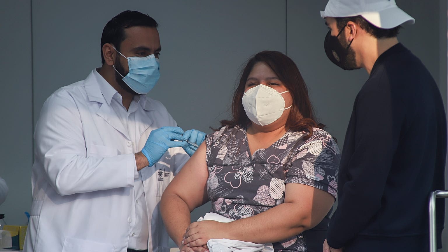El ministro de Salud de El Salvador, Francisco Alabi, procede a vacunar a una enfermera ante la mirada atenta del presidente, Nayib Bukele.