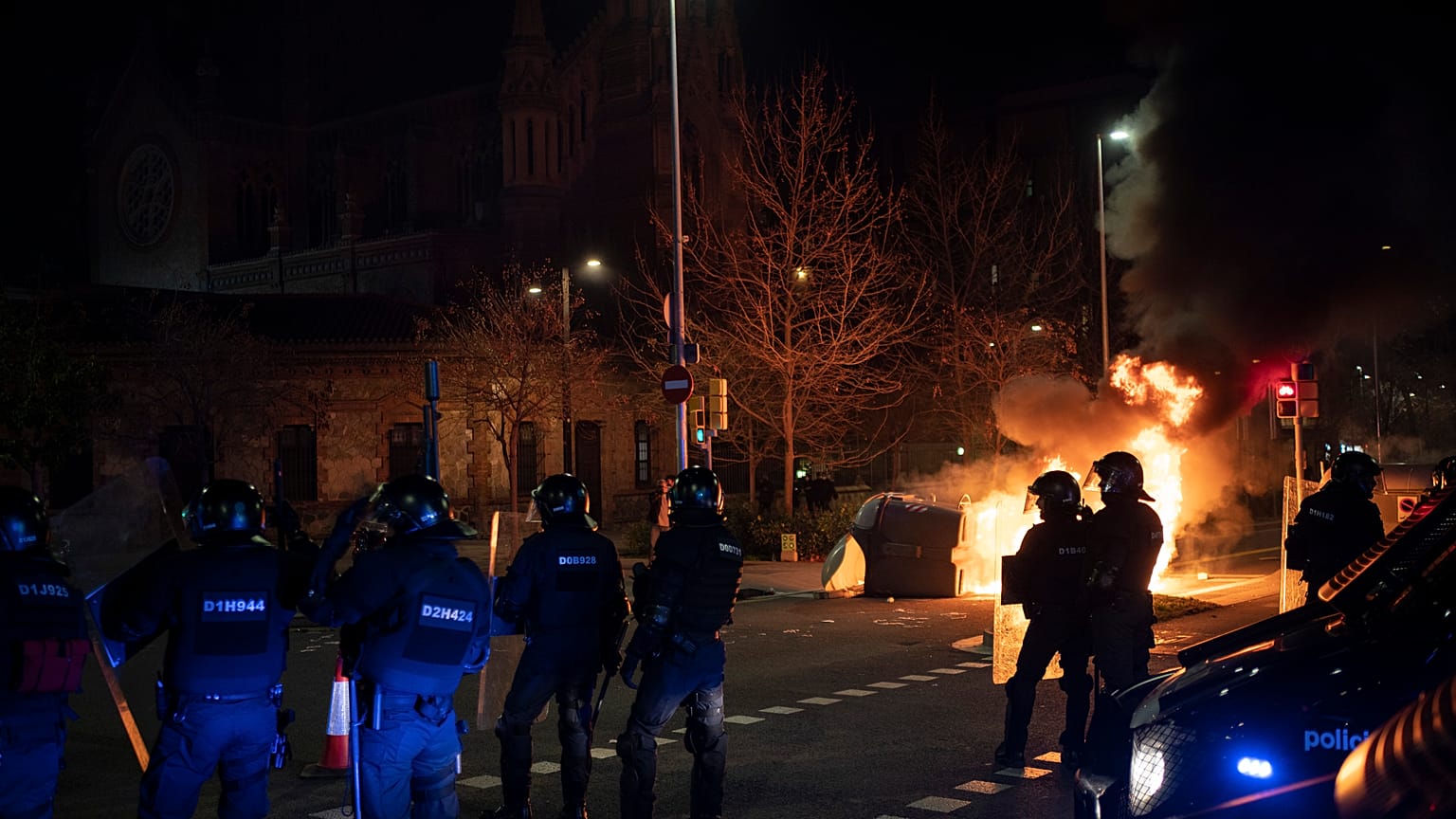 Police officers take position next to a burning barricade during clashes following a protest condemning the arrest of rap singer Pablo Hasél in Barcelona, Spain, Feb.18, 2021.