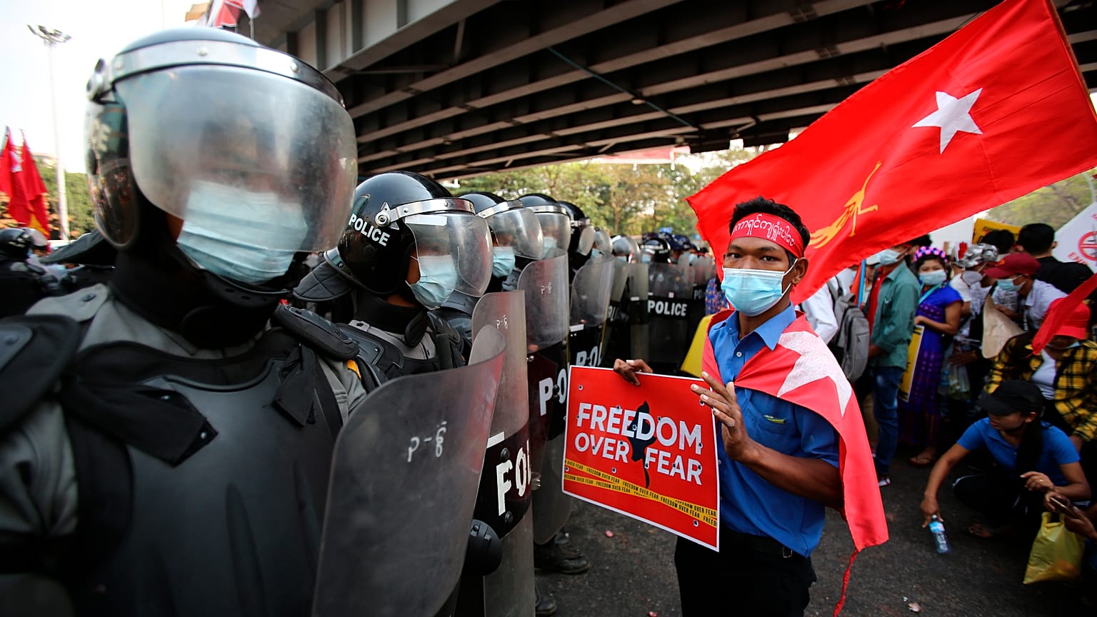 An anti-coup protester holds a poster as he stands in front of riot police in Yangon, Myanmar on Friday
