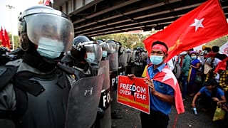 An anti-coup protester holds a poster as he stands in front of riot police in Yangon, Myanmar on Friday