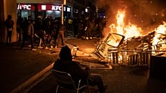 A man sits on a chair in front of a burning barricade during a protest condemning the arrest of rap singer Pablo Hasél in Barcelona, Spain, Friday, Feb. 19, 2021.