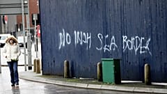 A woman walks past past graffiti with the words 'No Irish Sea Border' in Belfast city centre, Northern Ireland, Wednesday, Feb. 3, 2021. 