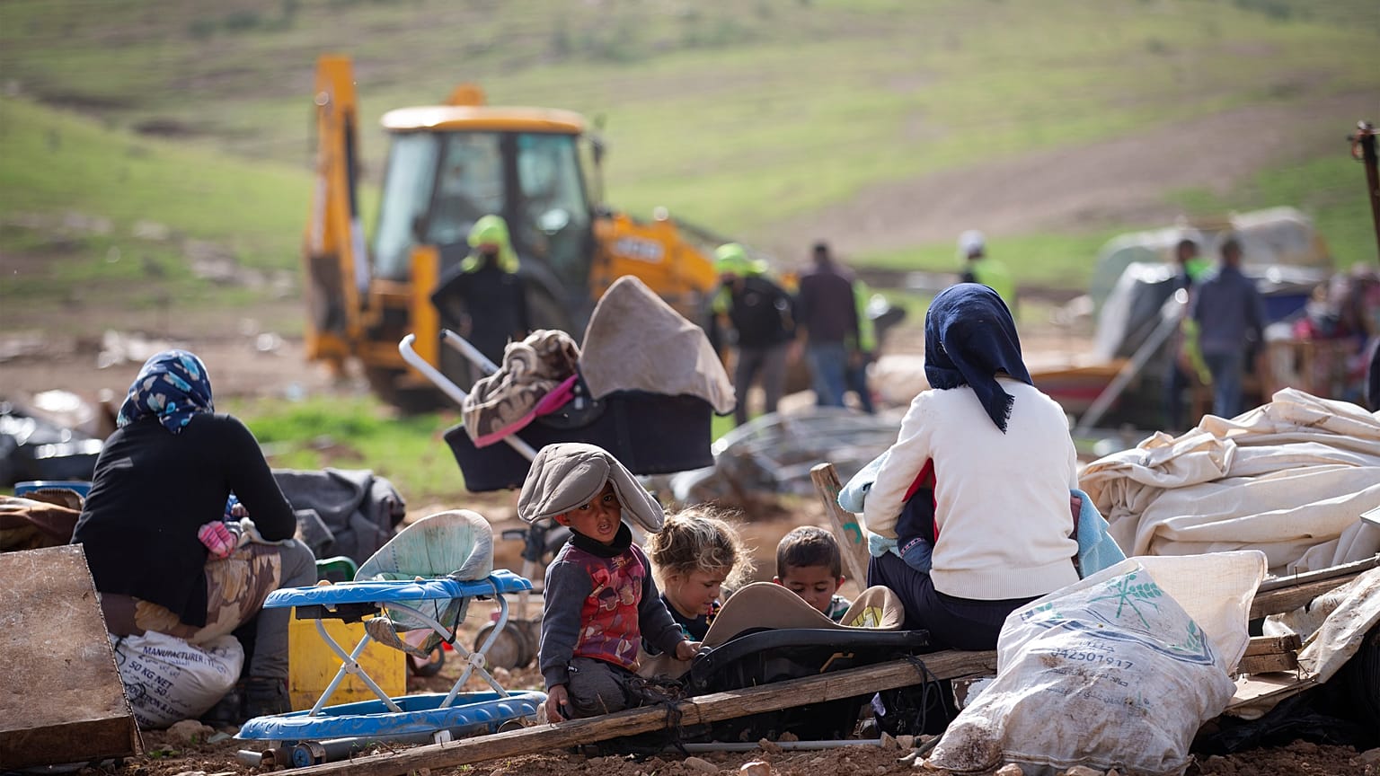 بدو فلسطينيون ينظرون إلى القوات الإسرائيلية  وهي تهدم الخيام وغيرها من المباني في قرية في غور الأردن بالضفة الغربية