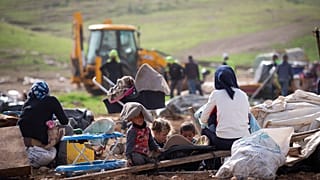 بدو فلسطينيون ينظرون إلى القوات الإسرائيلية  وهي تهدم الخيام وغيرها من المباني في قرية في غور الأردن بالضفة الغربية