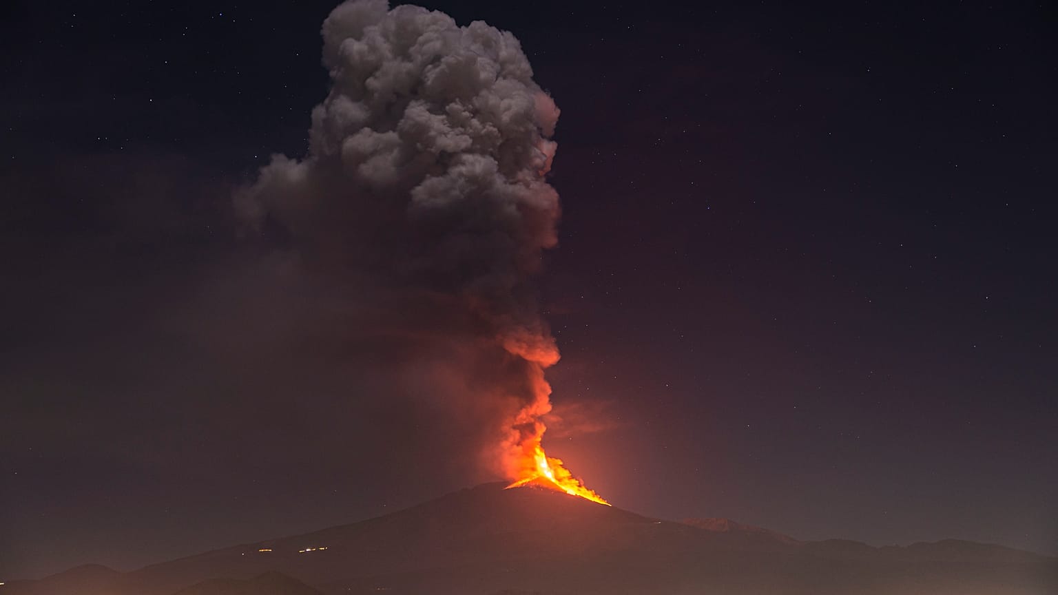 Flames and smoke billowing from a crater, as seen from the southern side of the Mt Etna volcano, tower over the city of Pedara, Sicily, Wednesday night, Feb. 24, 2021.