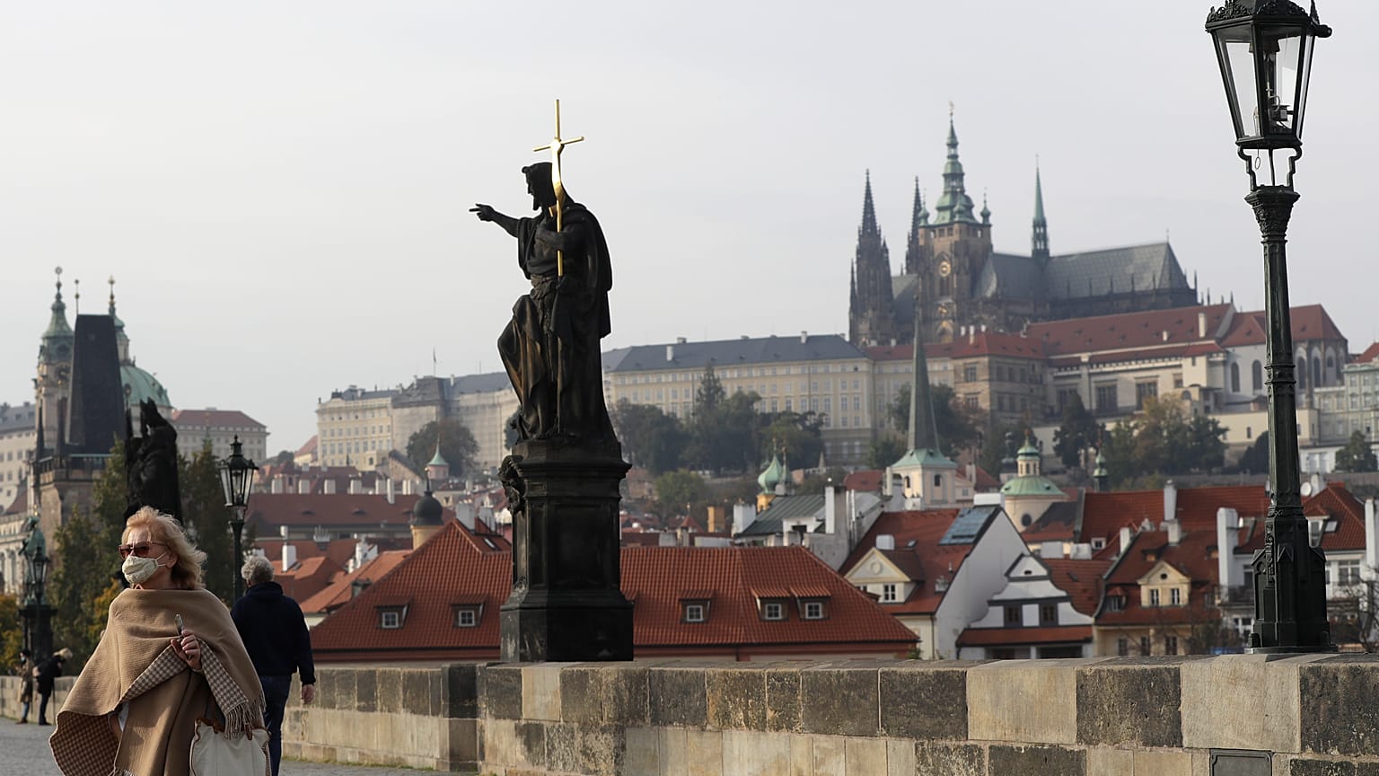 A woman wearing a face mask walks across the medieval Charles Bridge in Prague.