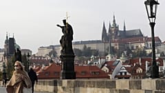 A woman wearing a face mask walks across the medieval Charles Bridge in Prague.