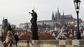 A woman wearing a face mask walks across the medieval Charles Bridge in Prague.