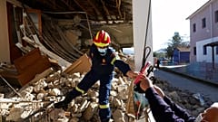 A firefighter inside a damaged house, gives a plastic bag with salvaged shoes to a man after an earthquake in Damasi villag