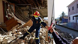 A firefighter inside a damaged house, gives a plastic bag with salvaged shoes to a man after an earthquake in Damasi villag