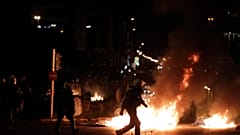 Αστυνομικός των ΜΑΤ περπατάει μπροστά από φωτιές 