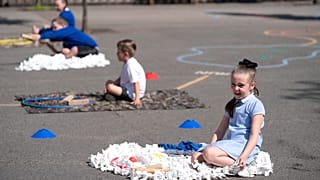 Children at Seymour Road Academy sit in designated areas in the playground during the coronavirus outbreak in Manchester, England, Wednesday May 20, 2020.