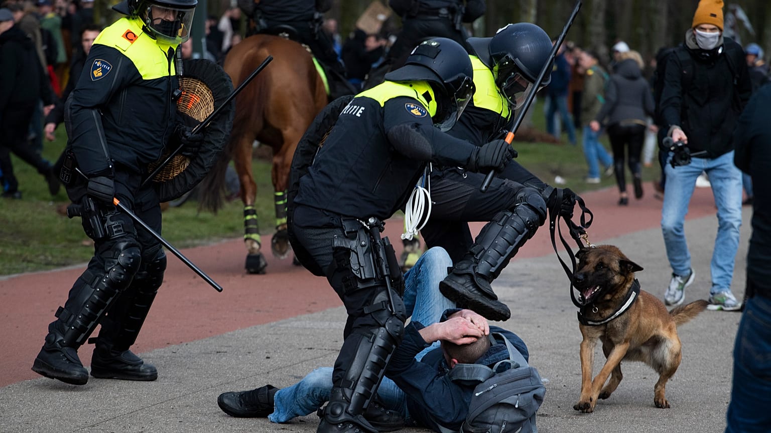 Dutch riot police kick a man during a demonstration to protest government policies including the curfew, lockdown and coronavirus related restrictions in The Hague.