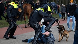 Dutch riot police kick a man during a demonstration to protest government policies including the curfew, lockdown and coronavirus related restrictions in The Hague.