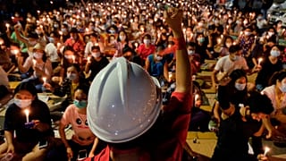 An anti-coup protester raises his hand with clenched fist in front of a crowd during a candlelight night rally in Yangon, Myanmar Sunday, March 14, 2021.