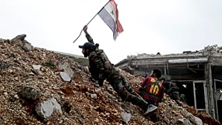 In this Dec. 5, 2016 file photo, a Syrian army soldier places a Syrian national flag during a battle with rebel fighters at the Ramouseh front line, east of Aleppo, Syria.