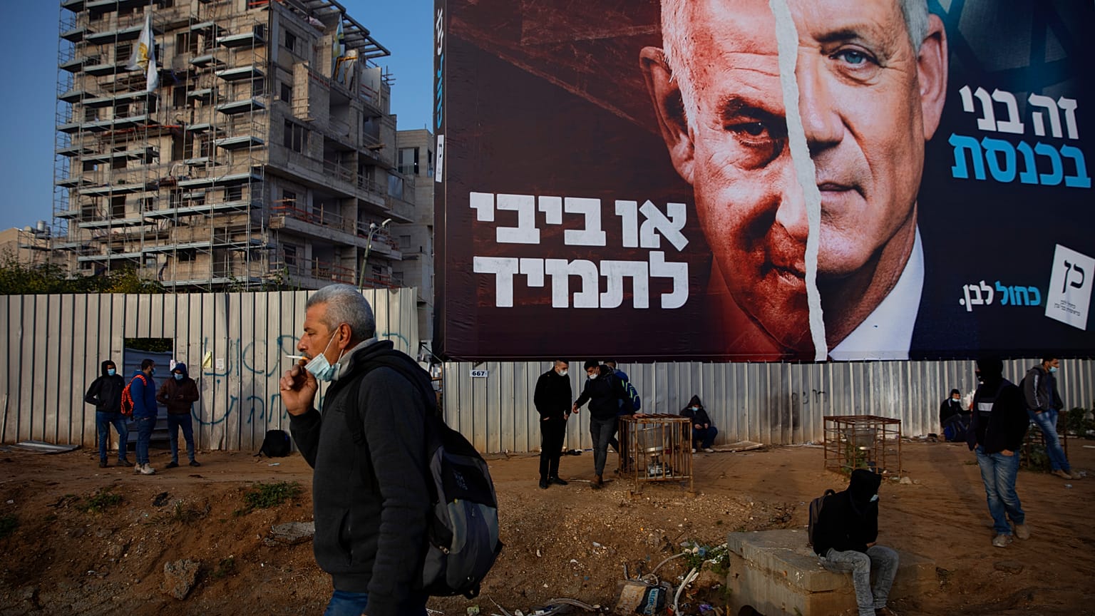فلسطينيون ينتظرون المواصلات تحت لوحة إعلانية لحملة الانتخابات الإسرائيلية. 2021/03/14