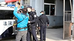 Security officers stand guard as a police van arrives at a court building in Dandong in northeastern China's Liaoning Province, Friday, March 19, 2021. 
