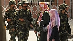 نساء مسلمات من الإيغور يسرن أمام الشرطة الصينية شبه عسكرية في أحد شوارع أورومتشي، عاصمة منطقة شينجيانغ الصينية.