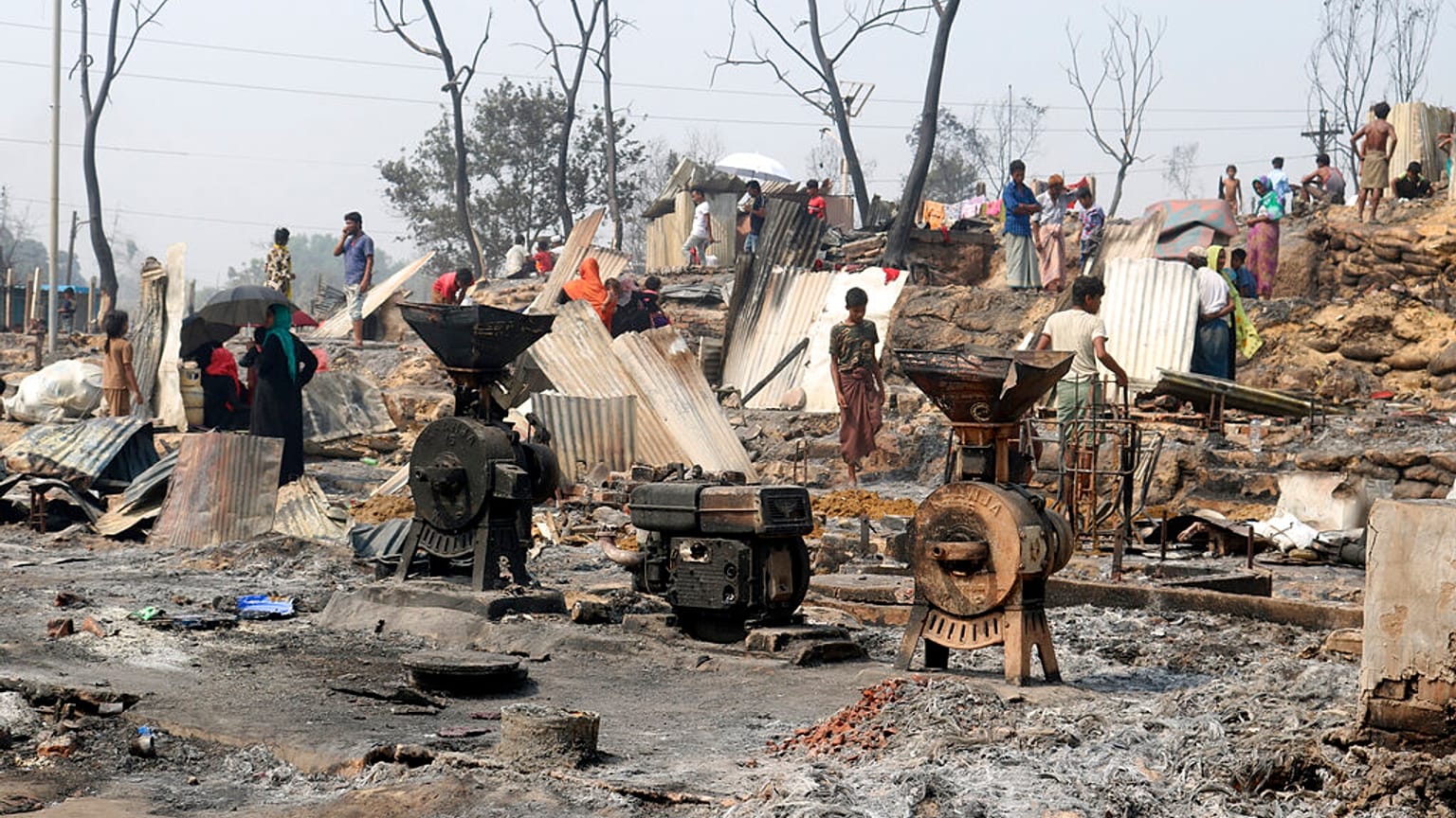 Rohingya refugees stand by remains of Monday's fire at a refugee camp in Balukhali, southern Bangladesh, Tuesday, March 23, 2021.