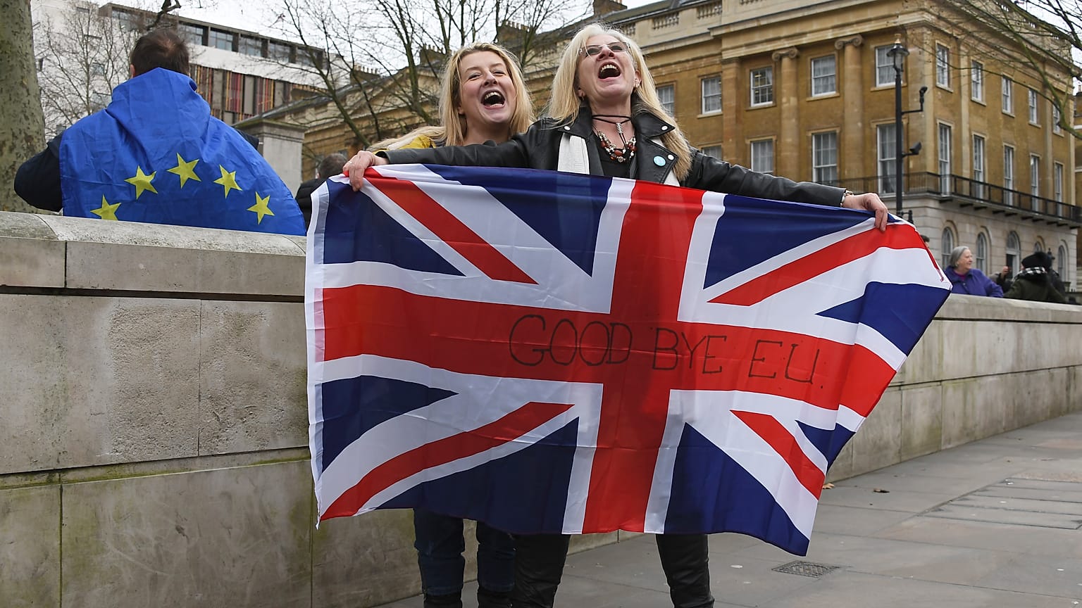 Brexit supporters hold the Union Jack with a text reading "Goodbye EU" as they celebrate next to a person wearing the EU flag in London, Friday, Jan. 31, 2020.