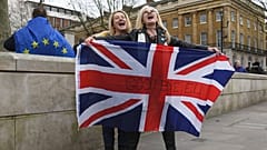 Brexit supporters hold the Union Jack with a text reading "Goodbye EU" as they celebrate next to a person wearing the EU flag in London, Friday, Jan. 31, 2020.