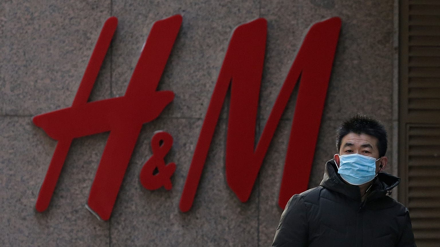 A man wearing a face mask walks by a Swedish fashion brand H&M store outlet in Beijing, March 25, 2021. 