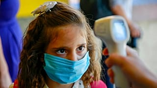 A pupil wearing a face mask to protect against coronavirus, has her temperature checked in the capital Pristina, Kosovo, Monday, Sept. 14, 2020.