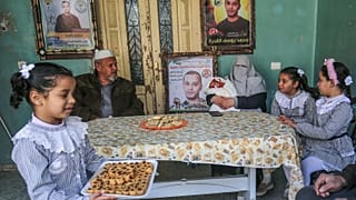 إيمان زوجة الأسير الفلسطيني محمد القدرة تحمل طفلها المولود حديثًا من حيوانات منوية مهربة مع والد زوجها وبناتها الثلاث في مخيم للاجئين في خان يونس جنوب غزة 