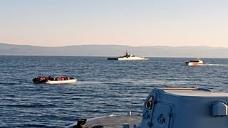 Yunan Sahil Güvenliği tarafından paylaşılan fotoğrafta, Midilli ile Türkiye kıyıları arasında, arka planda Türk gemileri ile solda göçmenlerin bulunduğu bir sandal görülüyor