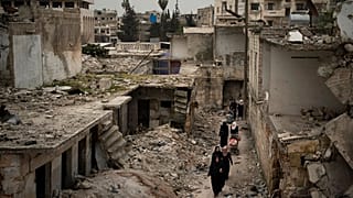 Suriye'nin İdlib kentinde hava bombardımanları sonucu yıkılan evlerin arasında yürüyen vatandaşlar