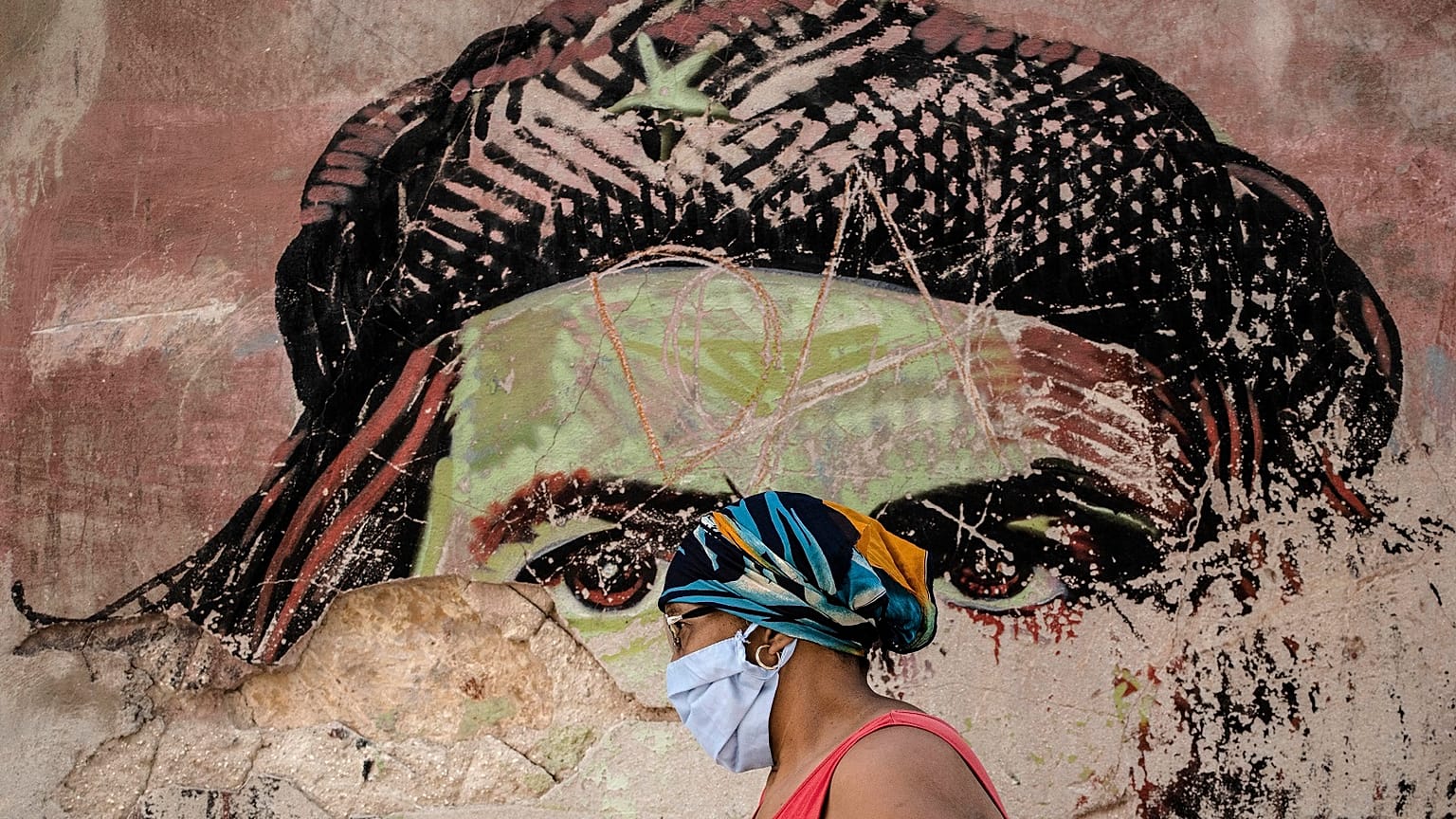 A woman wearing a protective face mask amid the new coronavirus pandemic, walks past a dilapidated mural featuring revolutionary hero Ernesto "Che" Guevara in Havana.