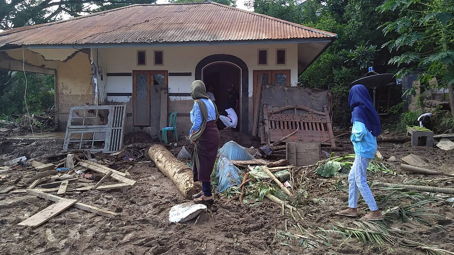 Indonesian women walk past a house damaged by flood in Waiwerang, on Adonara Island, East Nusa Tenggara province, Indonesia, Tuesday, April 6, 2021.