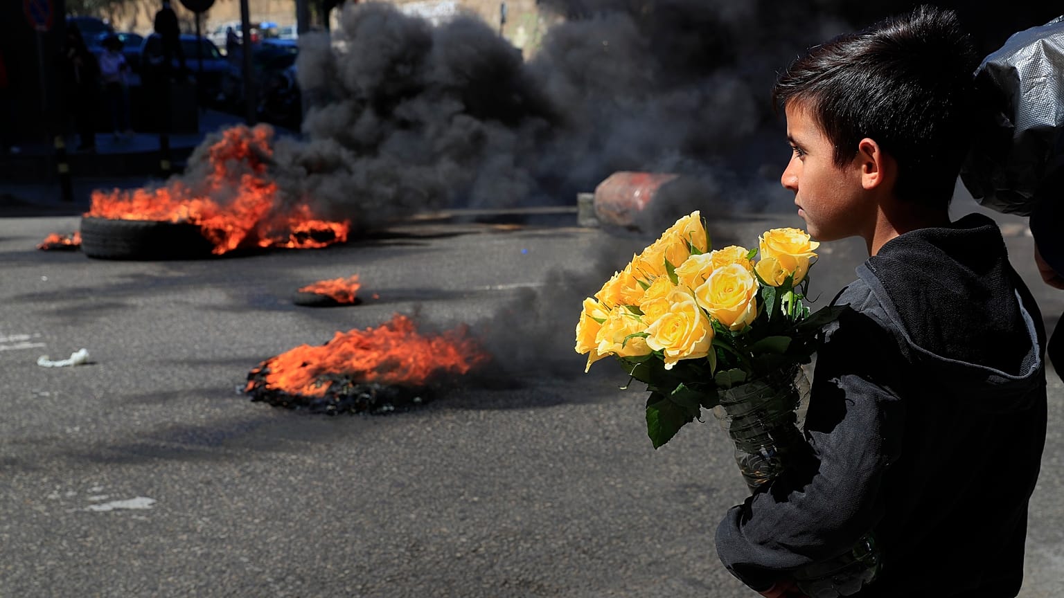 Un bambino siriano guarda i manifestanti che bruciano pneumatici per bloccare una strada principale durante una manifestazione a Beirut 