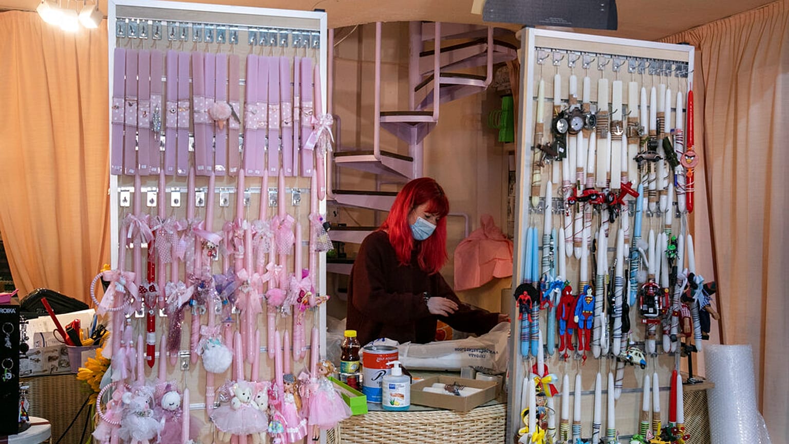 An employee, wearing a face mask to curb the spread of the coronavirus, works behind decorated candles for the Orthodox Easter