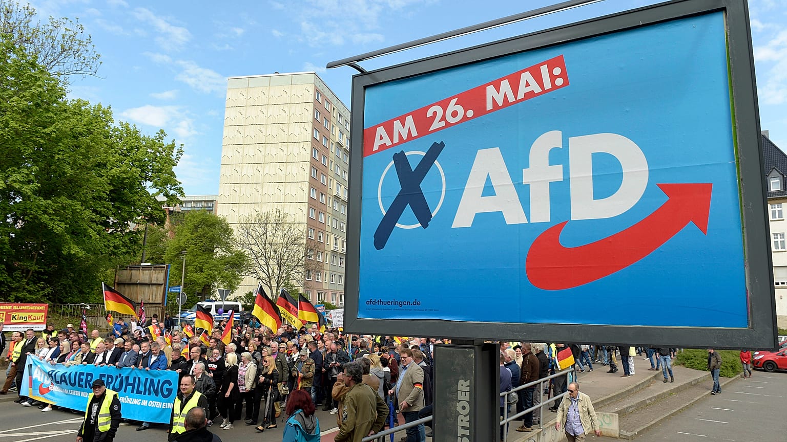 This picture taken May 1, 2019 shows AfD supporters walkin along a party elections poster in Erfurt, Germany. 