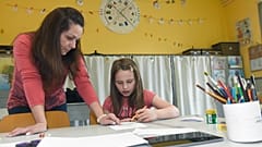 A teaching assistant helps a child with her assigment in a school in Budapest, Hungary Tuesday, March 31, 2020.