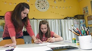 A teaching assistant helps a child with her assigment in a school in Budapest, Hungary Tuesday, March 31, 2020.