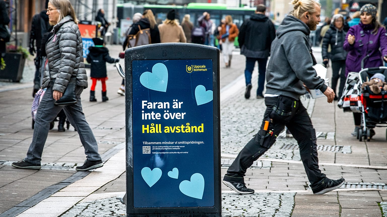 People walk past a bin with a sign reading "The danger is not over. Keep your distance" in a pedestrian street in central Uppsala, Sweden. October 21, 2020.