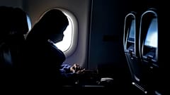 سيدة ترتدي كمامة وتجلس داخل طائرة